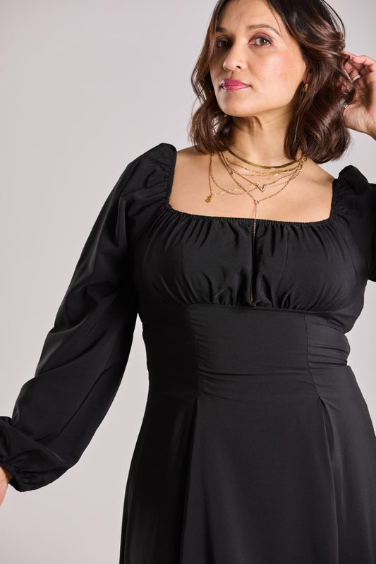Woman wearing a black dress with long sleeves against a plain background